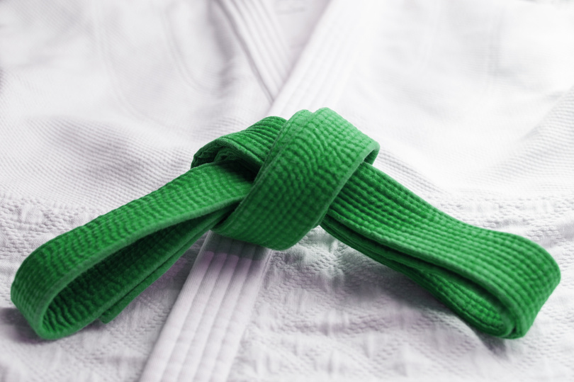 Green martial art belt tied in a knot on blue background